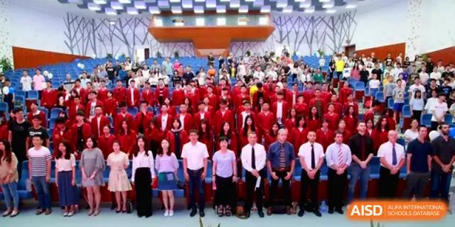 A large group of students in red graduation gowns pose for a group photo on a stage with faculty at Quanzhou No. 5 Middle School.