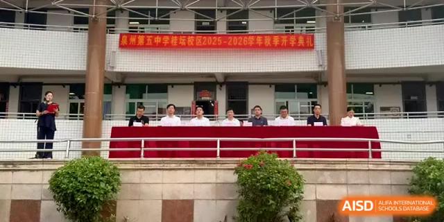 School officials sit at a long table on a balcony overlooking an outdoor school event or assembly at Quanzhou No. 5 Middle School.