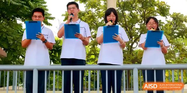 Two student emcees hold blue folders and speak into microphones during an outdoor school event at Quanzhou No. 5 Middle School.