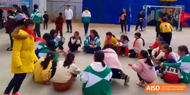 Students sit in a circle on an outdoor court, participating in a group discussion or team-building game at Quanzhou No. 5 Middle School.