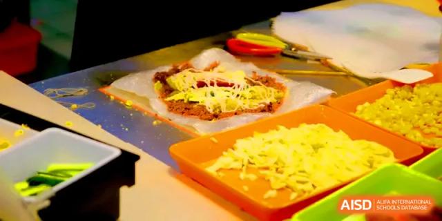 A chef prepares savory crepes or wraps with fresh ingredients on a flat grill in the kitchen at Quanzhou No. 5 Middle School.