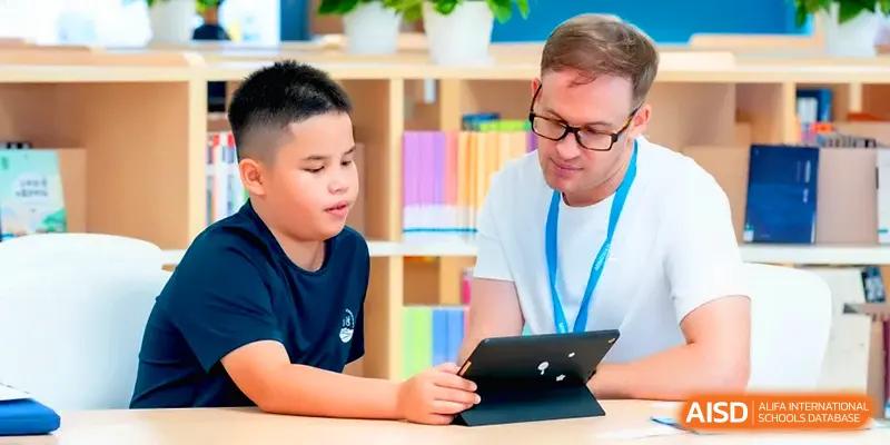 A teacher assists a young student with a digital tablet during a focused classroom session at Shenzhen Mingwan School.