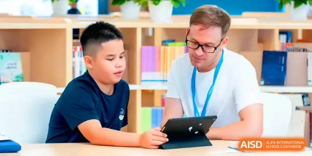 A teacher assists a young student with a digital tablet during a focused classroom session at Shenzhen Mingwan School.