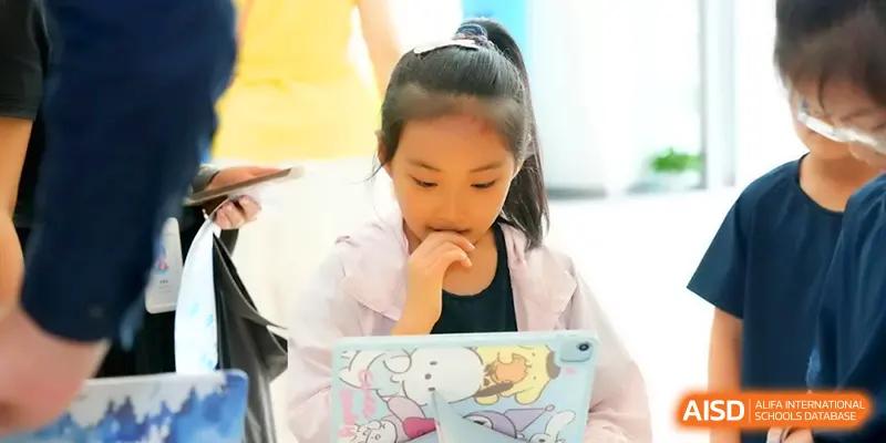 A young girl focused on her tablet during a digital learning session in a bright classroom at Shenzhen Mingwan School.