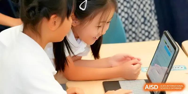 A young student smiles while working closely with a peer on a laptop during a collaborative task at Shenzhen Mingwan School.