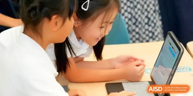 A young student smiles while working closely with a peer on a laptop during a collaborative task at Shenzhen Mingwan School.