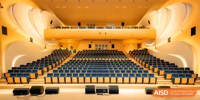 A wide shot of a large, empty school auditorium with rows of seating and stage lighting at Shenzhen Mingwan School.