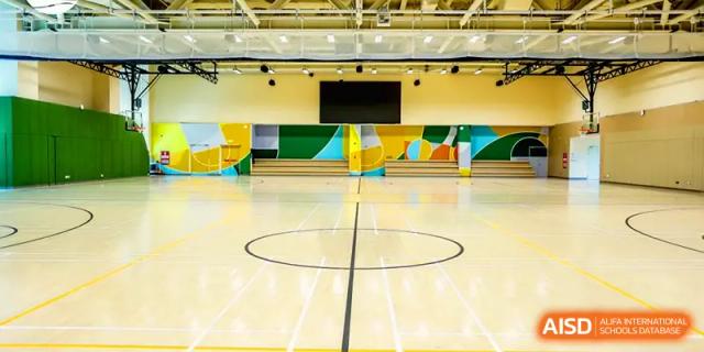 An expansive indoor gymnasium with polished wooden floors and basketball markings at Shenzhen Mingwan School.
