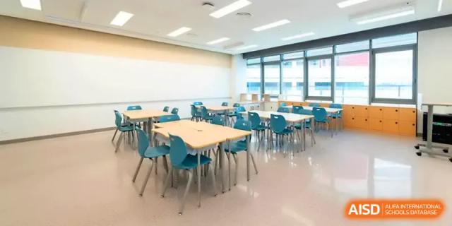 A modern classroom setup with light wood tables and blue chairs arranged for group work at Shenzhen Mingwan School.