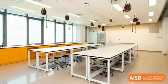 A clean and modern science laboratory with white benches and stools for experiments at Shenzhen Mingwan School.