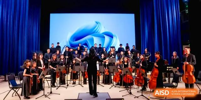 A conductor leads a youth orchestra and choir performing on a professional stage at Shenzhen Mingwan School.