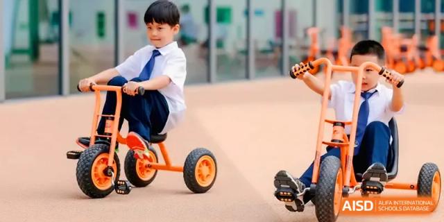 A young boy in a school uniform riding an orange tricycle in a safe play area at Shenzhen Mingwan School.