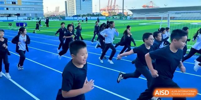 Energetic students running on a blue track during an outdoor sports event on the field at Shenzhen Mingwan School.