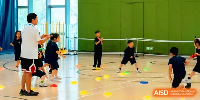 Children participating in a physical education class with yellow cones on a court at Shenzhen Mingwan School.
