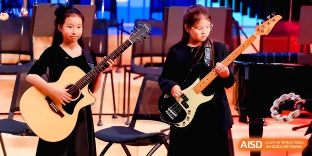 A young girl playing an electric bass guitar during a music performance on stage at Shenzhen Mingwan School.
