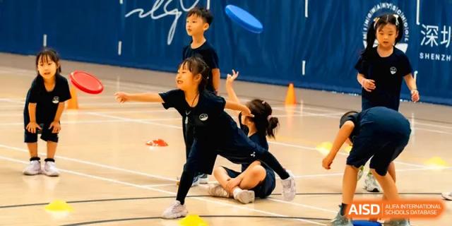 Young girl in school sports kit balances with one leg extended during a dance or PE class at Shenzhen Mingwan School.
