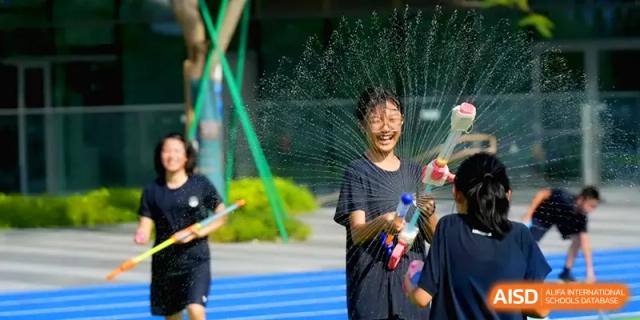 Students having fun with water guns, laughing as water sprays around them on a running track at Shenzhen Mingwan School.