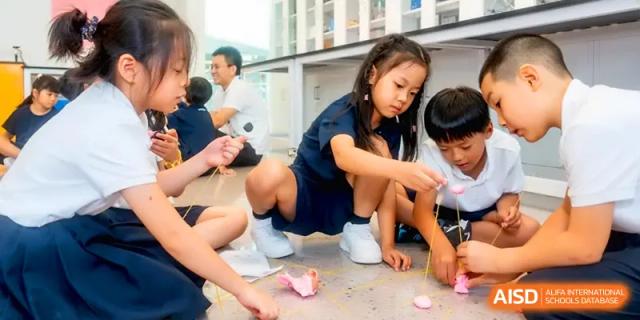 Students crouching on the floor, deeply focused on a detailed art or craft project at Shenzhen Mingwan School.