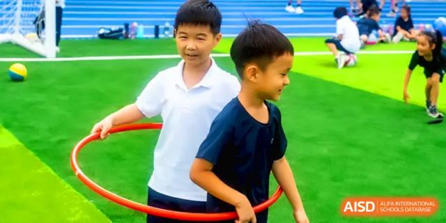 Two young boys in white and dark blue shirts playing and sharing a red hula hoop at Shenzhen Mingwan School.