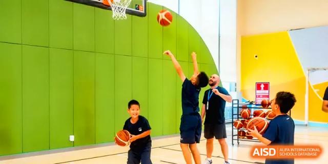 An instructor coaches a student taking a shot on an indoor basketball court at Shenzhen Mingwan School.