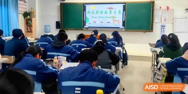A large group of students in blue uniforms listens to a presentation in a spacious classroom at The Guandu Experimental School Affiliated To Shanghai Normal University.