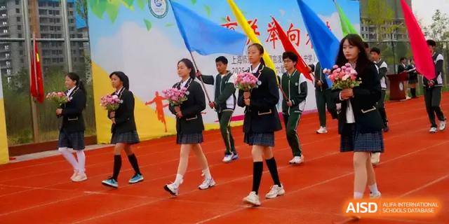 Students carry flowers and flags while walking on a red running track at The Guandu Experimental School Affiliated To Shanghai Normal University.