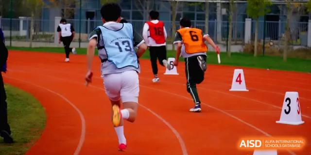 Students wearing numbered bibs compete in a relay race on a red running track at The Guandu Experimental School Affiliated To Shanghai Normal University.