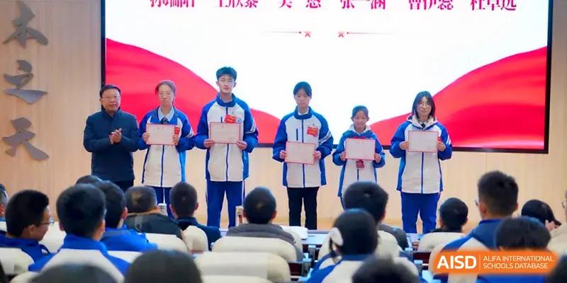A group of students stands at the front of a hall holding merit certificates for an awards ceremony at The Middle School Affiliated to Sichuan University.