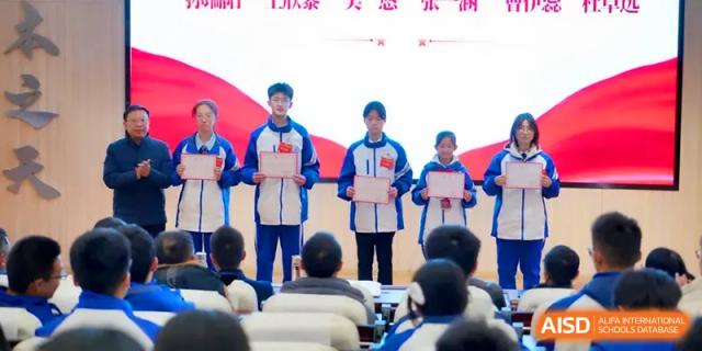 A group of students stands at the front of a hall holding merit certificates for an awards ceremony at The Middle School Affiliated to Sichuan University.