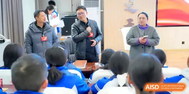 A staff member speaks into a microphone while addressing a seated group of students in a hall at The Middle School Affiliated to Sichuan University.