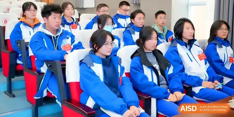 Students wearing matching blue jackets sit in tiered seating during an assembly or guest lecture at The Middle School Affiliated to Sichuan University.