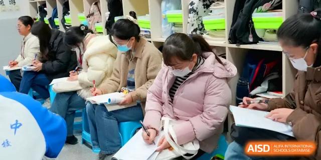 Two staff members in winter coats sit at desks while focused on their academic paperwork in class at The Middle School Affiliated to Sichuan University.