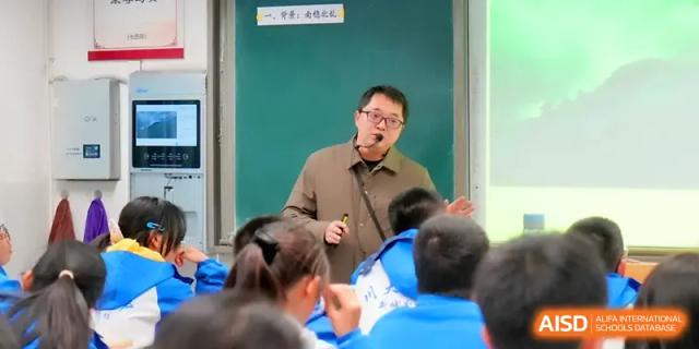 A male teacher in a brown coat delivers an engaging lecture at the front of a classroom for a group of students at The Middle School Affiliated to Sichuan University.