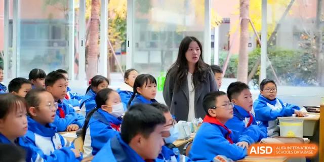 An instructor in a white coat stands attentively at the front of a modern classroom filled with students in blue jackets at The Middle School Affiliated to Sichuan University.