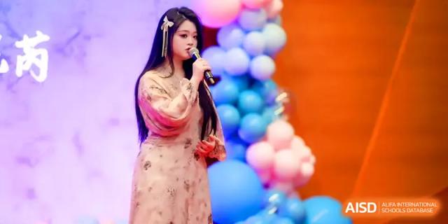 A young female student in a traditional floral dress sings into a microphone during a colorful stage performance at The Middle School Affiliated to Sichuan University.