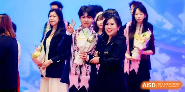 Two staff members smile while posing together with a bouquet of flowers after a successful school presentation at The Middle School Affiliated to Sichuan University.
