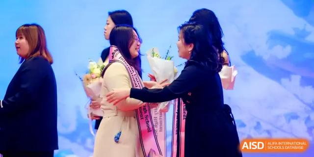 A teacher presents a bouquet of white flowers to a student on stage during a formal recognition ceremony at The Middle School Affiliated to Sichuan University.