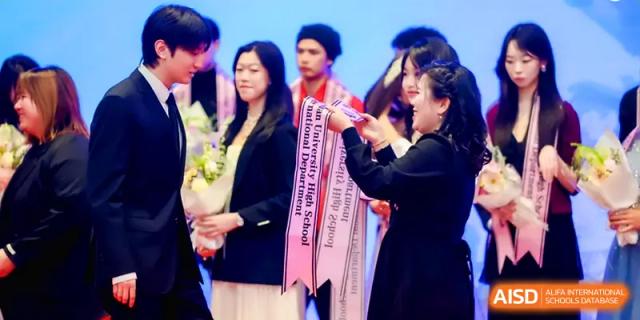 A staff member in a professional dark coat presents flowers to a student during a celebratory school event on stage at The Middle School Affiliated to Sichuan University.