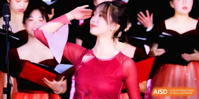 A female student in a vibrant red dress performs a traditional dance during a cultural arts performance on stage at The Middle School Affiliated to Sichuan University.