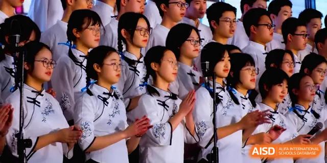 A group of female students in white traditional dresses performs a synchronized choral piece on stage at The Middle School Affiliated to Sichuan University.