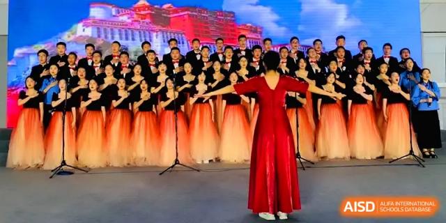 A female conductor in a red dress leads a large student choir during an outdoor evening performance at The Middle School Affiliated to Sichuan University.