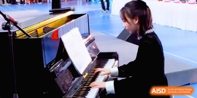 A female student plays a black grand piano with focus and skill during a musical recital held at The Middle School Affiliated to Sichuan University.