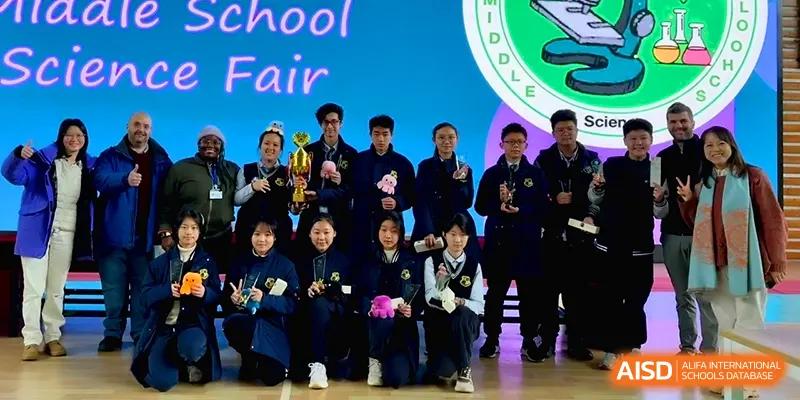 A group of students in navy uniforms poses with trophies and awards in front of a Science Fair banner at Xiwai International School.