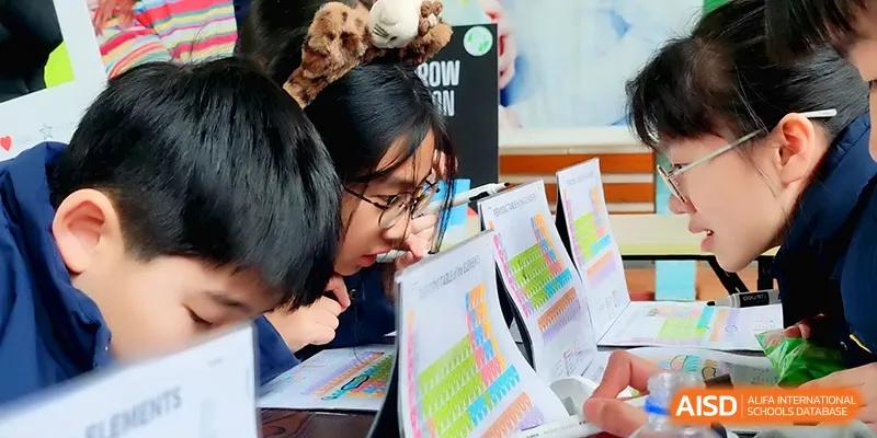 Two students look closely at a periodic table chart and science project materials at Xiwai International School.