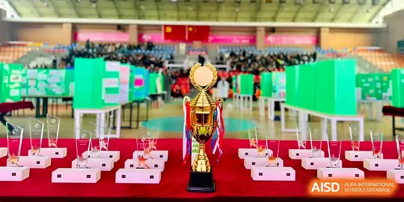 A gold trophy with red ribbons sits prominently on a table in a large gymnasium at Xiwai International School.