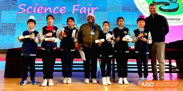 Students stand on stage with a teacher during an awards ceremony at a school science fair at Xiwai International School.