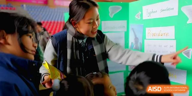 A smiling student points to her green science project display board during a school fair at Xiwai International School.