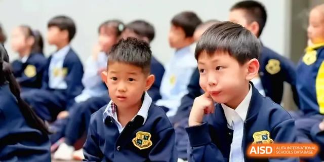 A group of young students in school uniforms sits together listening to a lesson at Xiwai International School.