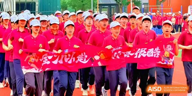 A spirited group of students in red uniforms runs together while holding a large red ceremonial banner at Xiwai International School.