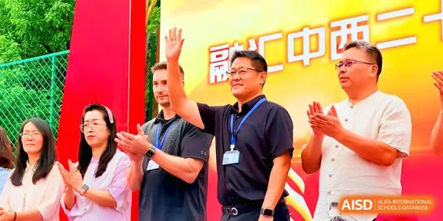 A school official in a black polo shirt waves to the crowd during an outdoor celebratory event at Xiwai International School.